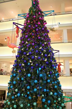 a large christmas tree in the middle of a mall with flamingos hanging from it's sides