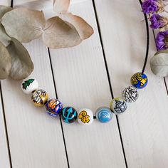 an assortment of colorful beads on a white wooden table next to plants and flowers with leaves