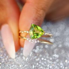 a woman's hand holding an engagement ring with a green gemstone