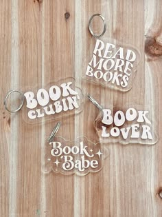 three clear book club keychains sitting on top of a wooden table