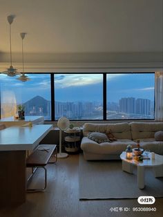 a living room filled with furniture and large windows overlooking the cityscape at dusk