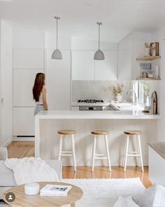 a woman is standing in the kitchen looking at the counter and stools that are on the floor