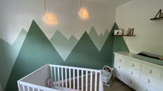 a baby's room with mountains painted on the wall and crib next to it