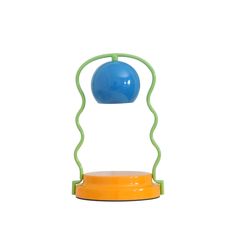 an orange and blue table lamp sitting on top of a wooden stand with a green base