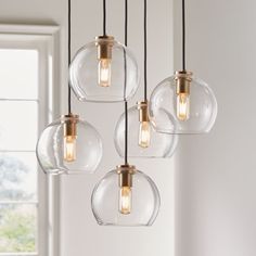 five clear glass globe pendant lights hanging from a ceiling fixture in a room with white walls and windows