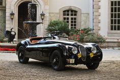 an old fashioned black sports car parked in front of a building