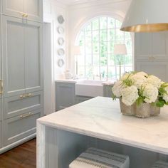 a large kitchen with marble counter tops and gray cabinets, white flowers in a basket on the island