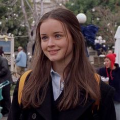 a girl with long hair and blue eyes smiles at the camera in front of an outdoor event