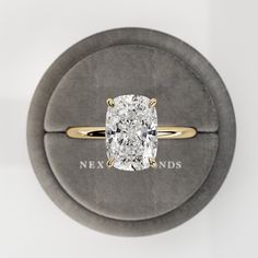 a ring with a cushion cut diamond in the center on a gray velvet box that says nexundds