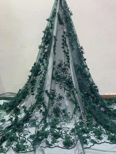 a white and green wedding dress with flowers on the bottom, in front of a wall