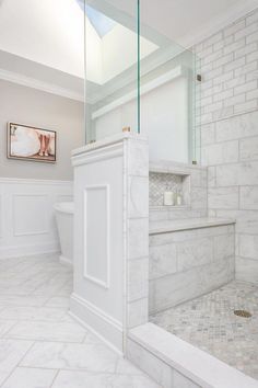 a white bathroom with marble tile flooring and walls, along with a walk in shower