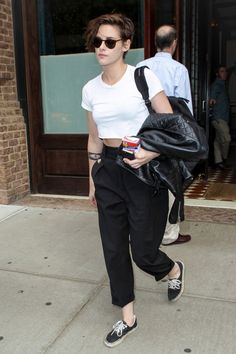 a woman in white shirt and black pants walking down street with handbag on back