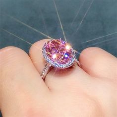 a close up of a person's hand holding a ring with a pink diamond