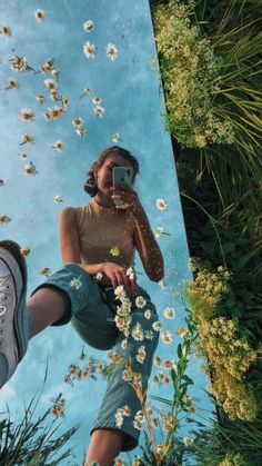 a woman taking a selfie with her cell phone in front of flowers and grass