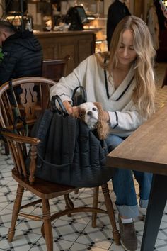 a woman sitting at a table with a dog in her lap and purse over her shoulder