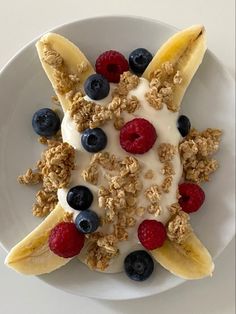 a white plate topped with granola, fruit and yogurt on top of banana slices