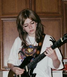 a young woman playing an electric guitar in front of wooden paneled walls and cupboards