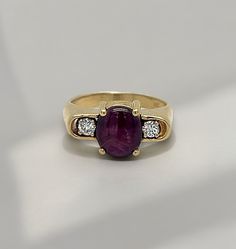 This beautiful estate piece features a round 1.89 ct cabochon ruby center stone and two round natural diamonds which total 0.15 ct. Set in 14k yellow gold. Ring can be sized upon purchase. Oval Cabochon Ruby Ring With Diamonds, Oval Cabochon Ruby And Diamond Ring, Luxury Oval Three-stone Ruby Ring, Classic Yellow Gold Three Stone Ruby Ring, Classic Three Stone Ruby Ring In Yellow Gold, Classic Three Stone Round Ruby Ring, Classic Three Stone Yellow Gold Ruby Ring, Cabochon Ruby Ring For Anniversary, Yellow Gold Ruby Ring With Oval Cabochon