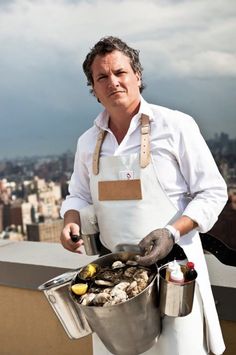 a man in an apron holding a bucket full of oysters on top of a building