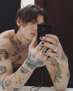 a man with tattoos is looking at his cell phone while sitting in front of a mirror