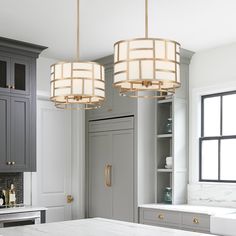 two chandeliers hanging from the ceiling in a kitchen with gray cabinets and marble counter tops