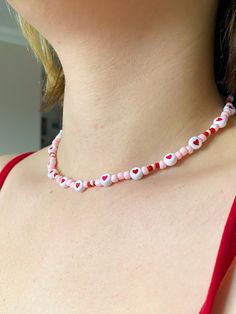 a woman wearing a pink and white beaded necklace with hearts on the bottom of it