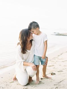 a woman kneeling down next to a little boy on the beach