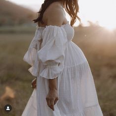 a woman in a white dress walking through a field