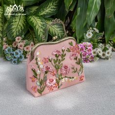 a pink purse sitting on top of a table next to flowers and greenery in the background