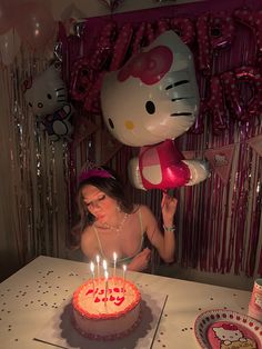 a woman blowing out candles on a cake with hello kitty balloons in the air behind her