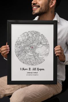 a man holding up a framed map with the words where it all begins in black and white