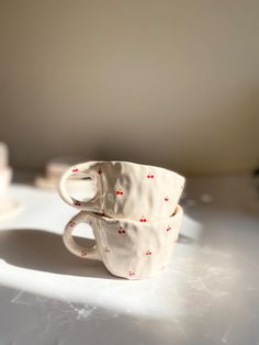 two coffee cups sitting on top of a table next to each other with red dots