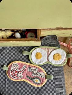 two fried eggs are sitting on top of a checkered table cloth and some other items