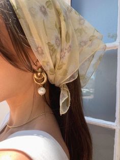 a woman wearing a white top and a yellow scarf on her head with earrings in front of a window