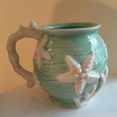 a ceramic mug with two starfishs on the handle and bottom, sitting on a table