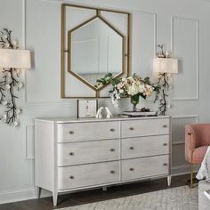 a white dresser with flowers on top and a large mirror above it in a room