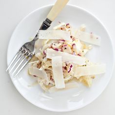 a white plate topped with pasta and cheese next to a fork on a table top