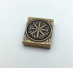 a gold and black square brooch with an intricate design on the front, sitting on a white surface