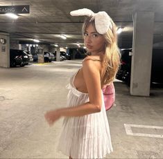 a woman in a parking garage wearing a white dress and bunny ears on her head