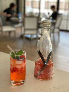 two drinks sitting on top of a table next to each other in front of a bottle