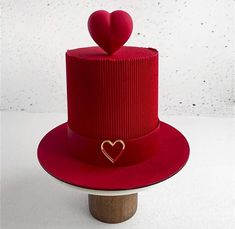 a red hat with a heart decoration on the top and a wooden stand underneath it