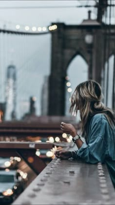 a woman is looking at her cell phone while standing on a bridge overlooking the city