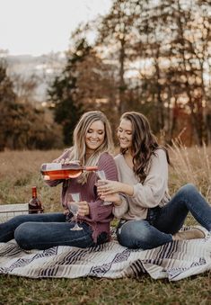 two women sitting on a blanket holding wine glasses