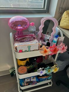 a white cart filled with lots of different items next to a mirror and window sill