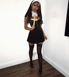 a woman dressed as a nun holding a cross in her hand while standing next to a wall