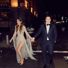 a man in a tuxedo and a woman in a dress walking down the street