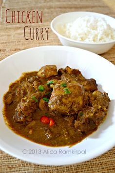 a white plate topped with chicken curry next to a bowl of rice and a spoon