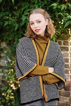 a woman standing in front of a brick wall wearing a black and white checkered coat