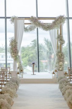 the aisle is decorated with white flowers and greenery for an elegant wedding ceremony in front of large windows