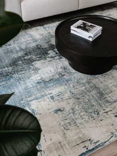 a coffee table with a book on it in front of a white couch and plant